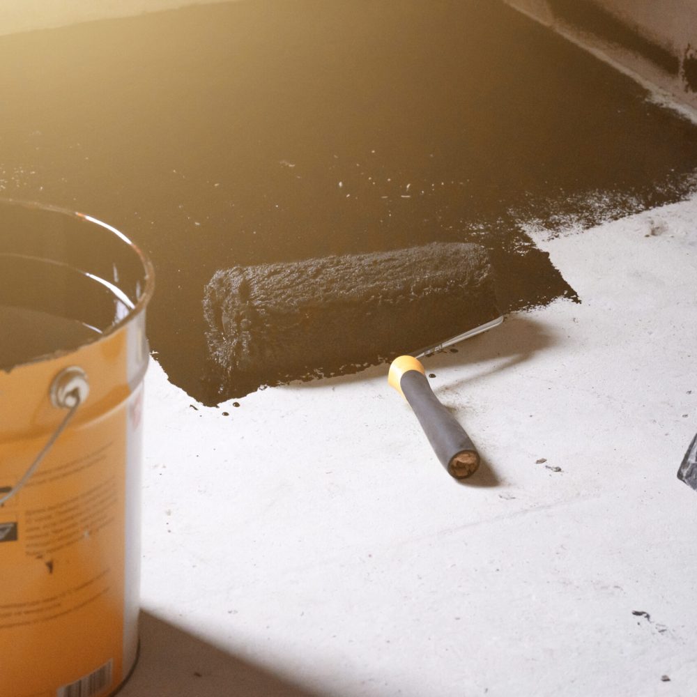 Applying hot resin to the floor for waterproofing, roller and bucket of resin, black and liquid resin.